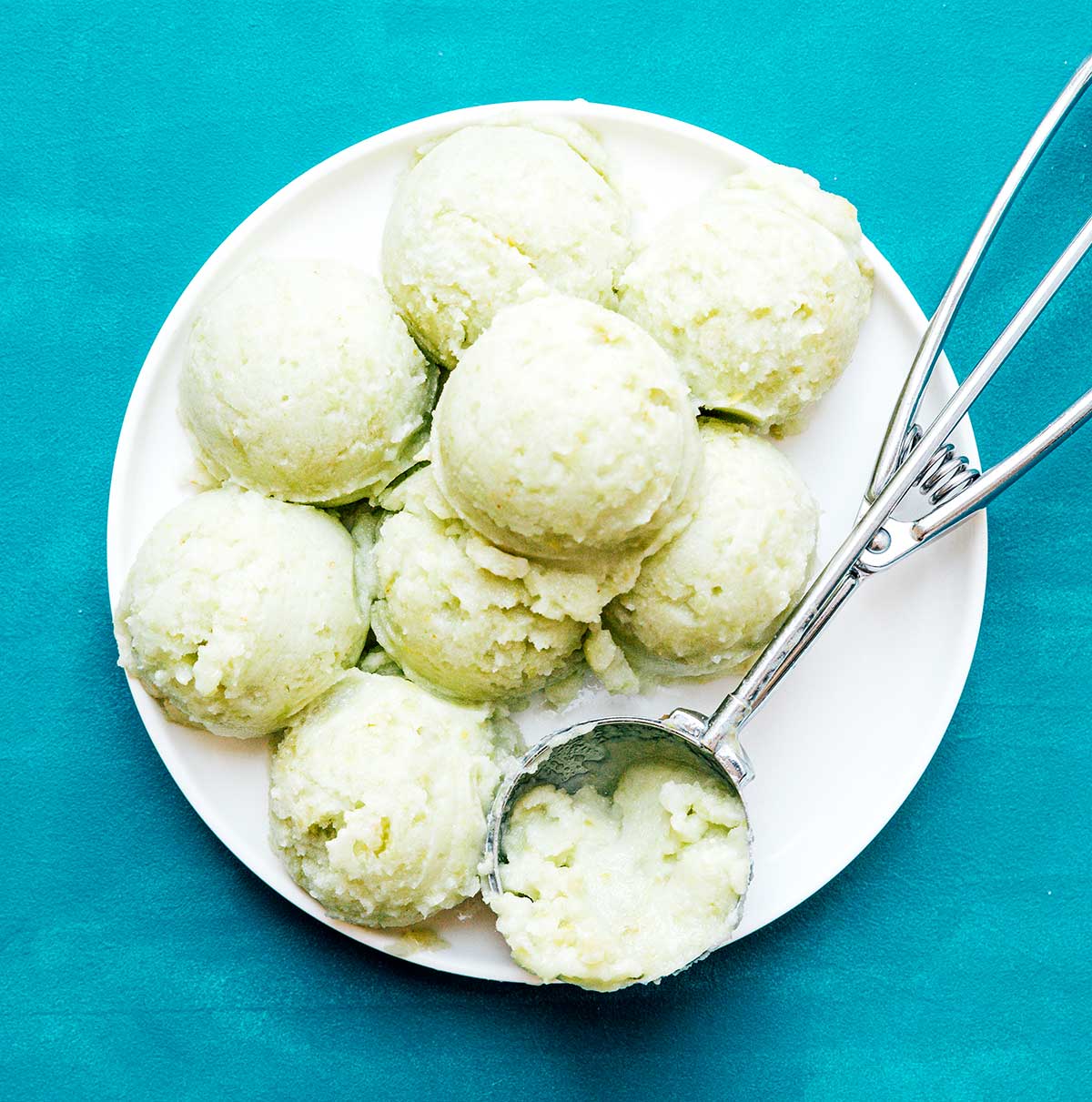 Frozen green seedless grape sorbet in white bowl with silver ice cream scoop inside bowl