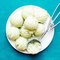 Frozen green seedless grape sorbet in white bowl with silver ice cream scoop inside bowl